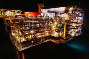 Oil rig/platform at night illuminated on all decks with scaffolding visible that hints to ongoing maintenance