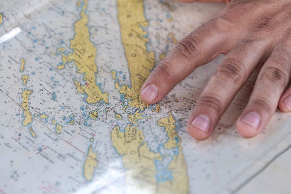 Photograph of a navigational chart with navigating officer's hand checking the chart to sail through safe waters